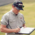 A man in a cap and sunglasses writing on a clipboard outdoors, pest control technician inspecting and filling out forms.