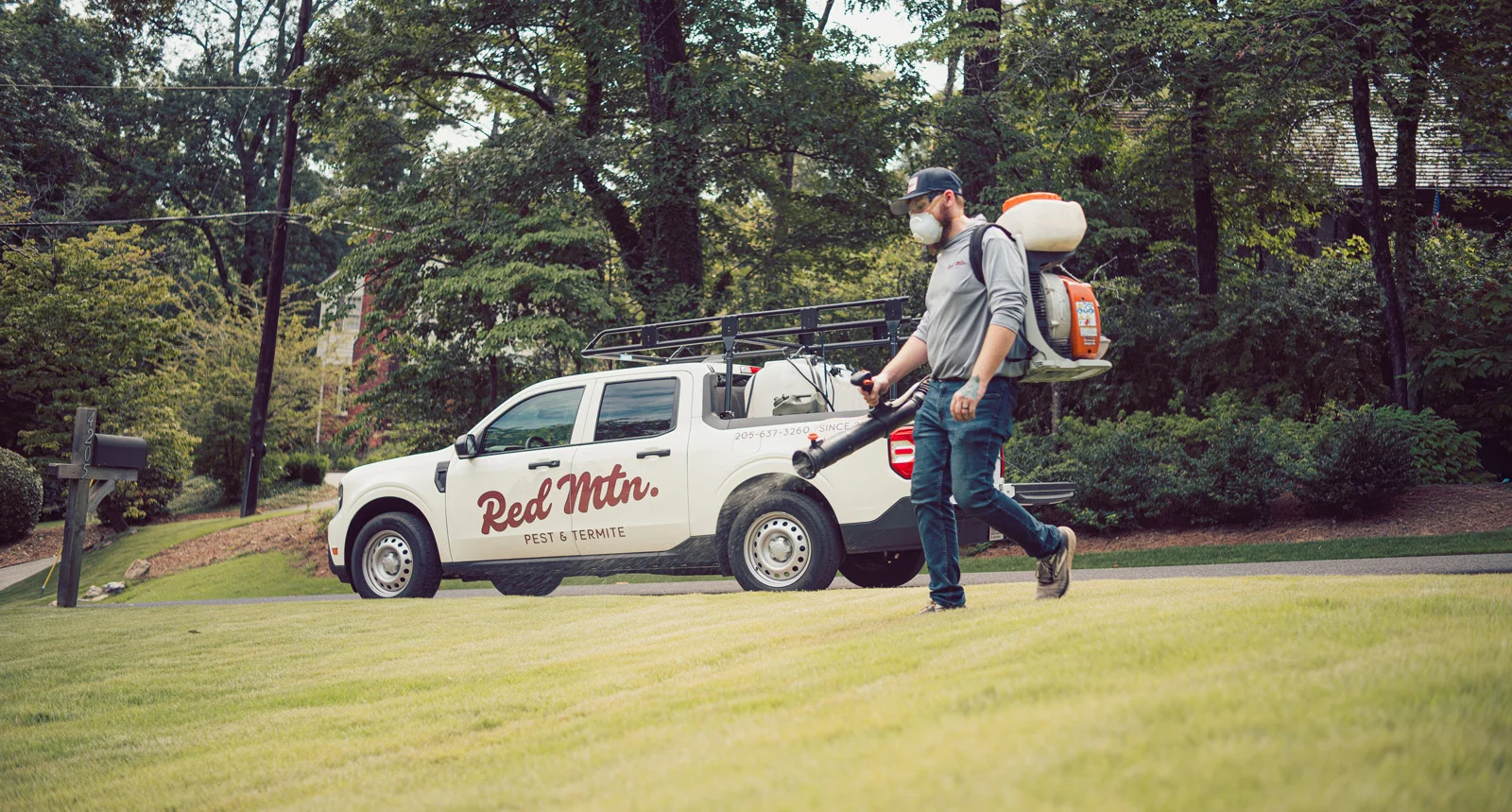 A pest control technician with backpack sprayer near Red Mtn. Pest & Termite truck on residential lawn