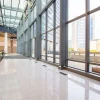 Spacious modern office atrium with floor-to-ceiling glass windows, reflective tiled floor and urban skyline view