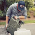 A man pouring water from a 20L olive green jerry can into a white container beside a pickup truck