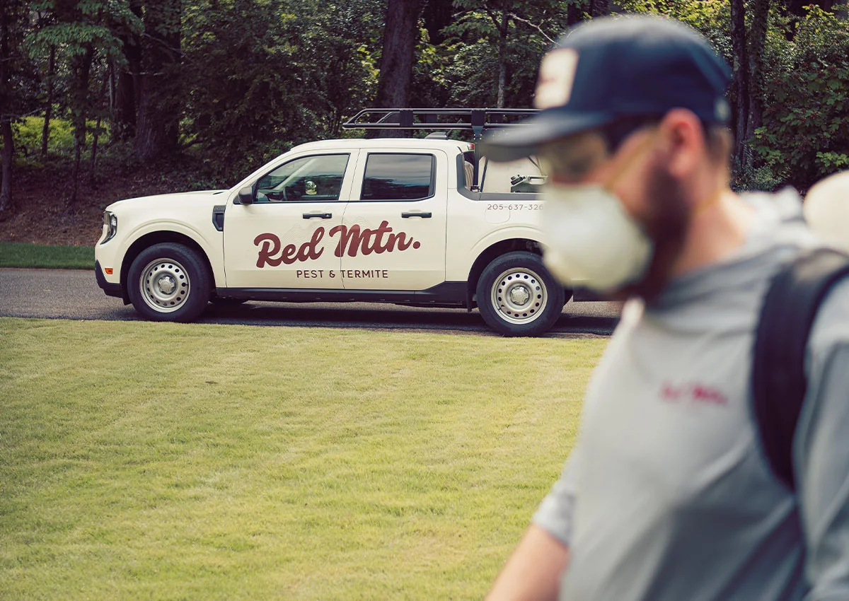 Red Mtn. Pest & Termite truck parked on a lawn with a masked pest-control technician in the foreground