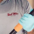 A person wearing Red Mtn. Pest & Termite shirt and blue glove holding a pest control treatment wand