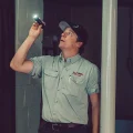 Home inspector examining basement ceiling with flashlight, wearing uniform shirt and cap