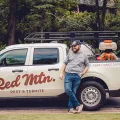 Pest control technician leaning on Red Mtn. Pest & Termite service truck with equipment