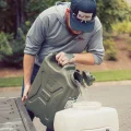 Man pouring water from 20L jerry can into a white container on a truck tailgate outdoors