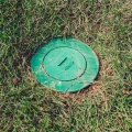 Green irrigation valve box cover set flush in patchy lawn grass for sprinkler system access