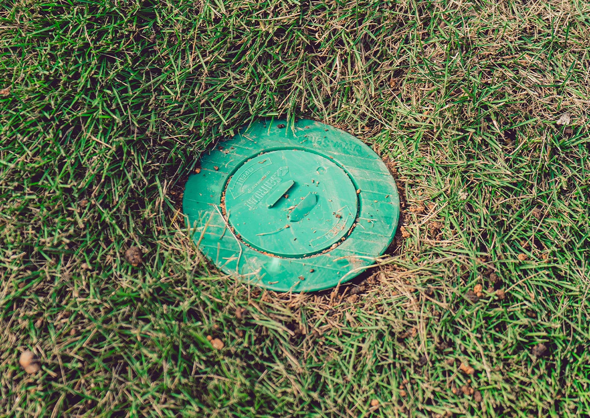 Green irrigation valve box cover set flush in patchy lawn grass for sprinkler system access