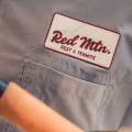 Close-up of pest control uniform with Red Mtn. Pest & Termite embroidered patch on gray shirt and tool handle