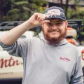 Smiling pest control technician tipping his cap, man in Red Mtn. shirt standing outdoors with service truck in background