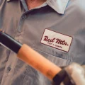 A person wearing a gray pest control uniform with 'Red Mtn Pest & Termite' patch, holding pest control equipment.