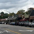 Small-town main street with local shops, pharmacy storefronts and parked cars under overcast sky