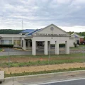 Trussville Municipal Building exterior with covered entrance, parking area, chain-link fence and cloudy sky.